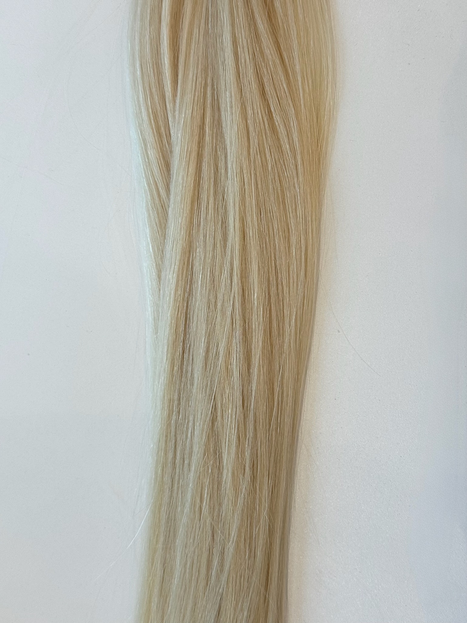 A long strand of straight, light blonde Frannie hair lies against a plain white background.
