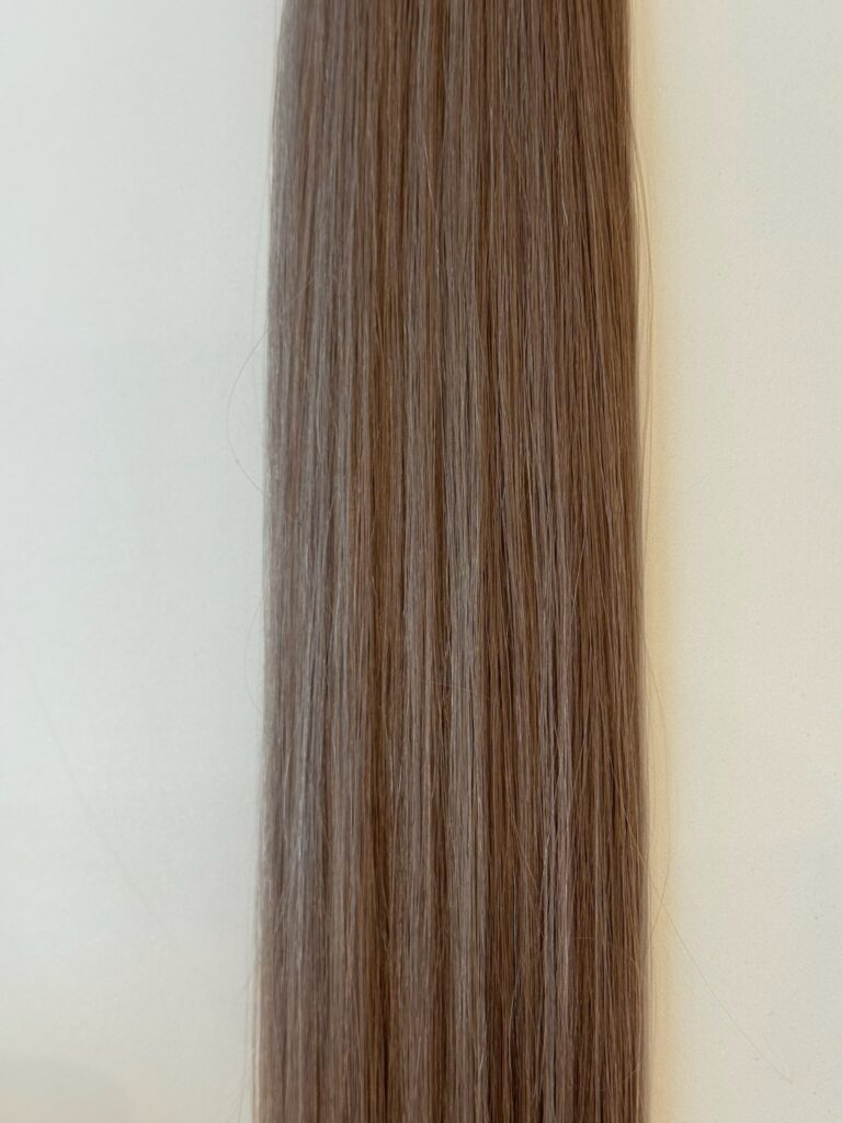 A close-up of Jessica's straight, light brown hair strands laid flat against a neutral, off-white background.