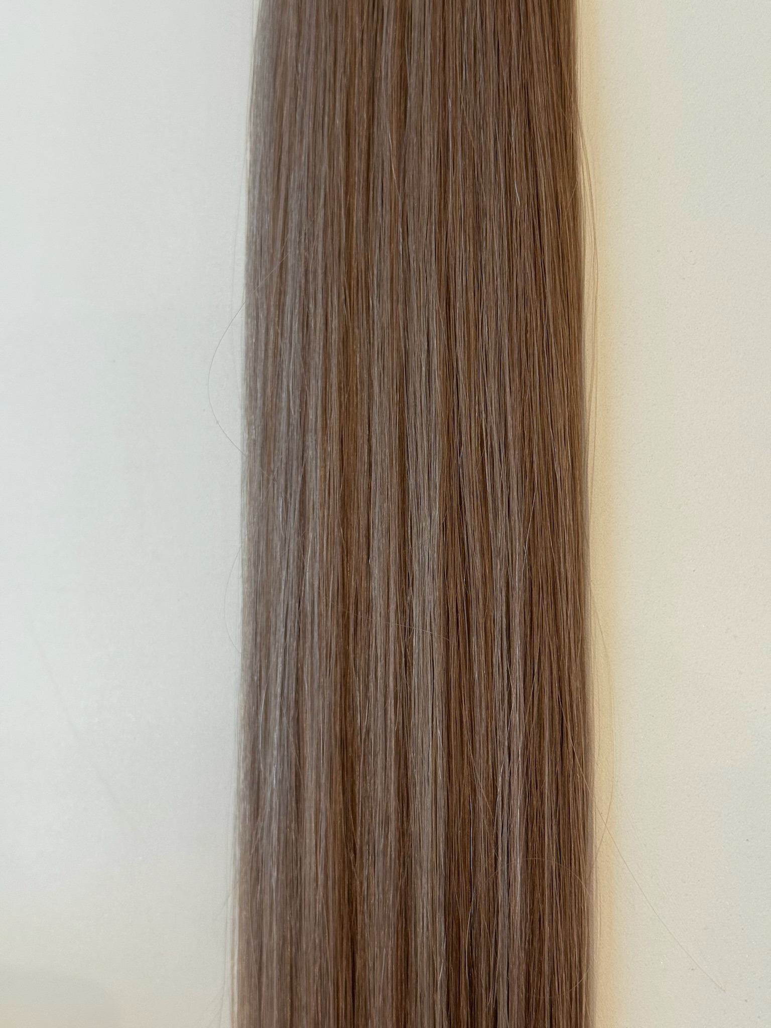 A close-up of Jessica's straight, light brown hair strands laid flat against a neutral, off-white background.
