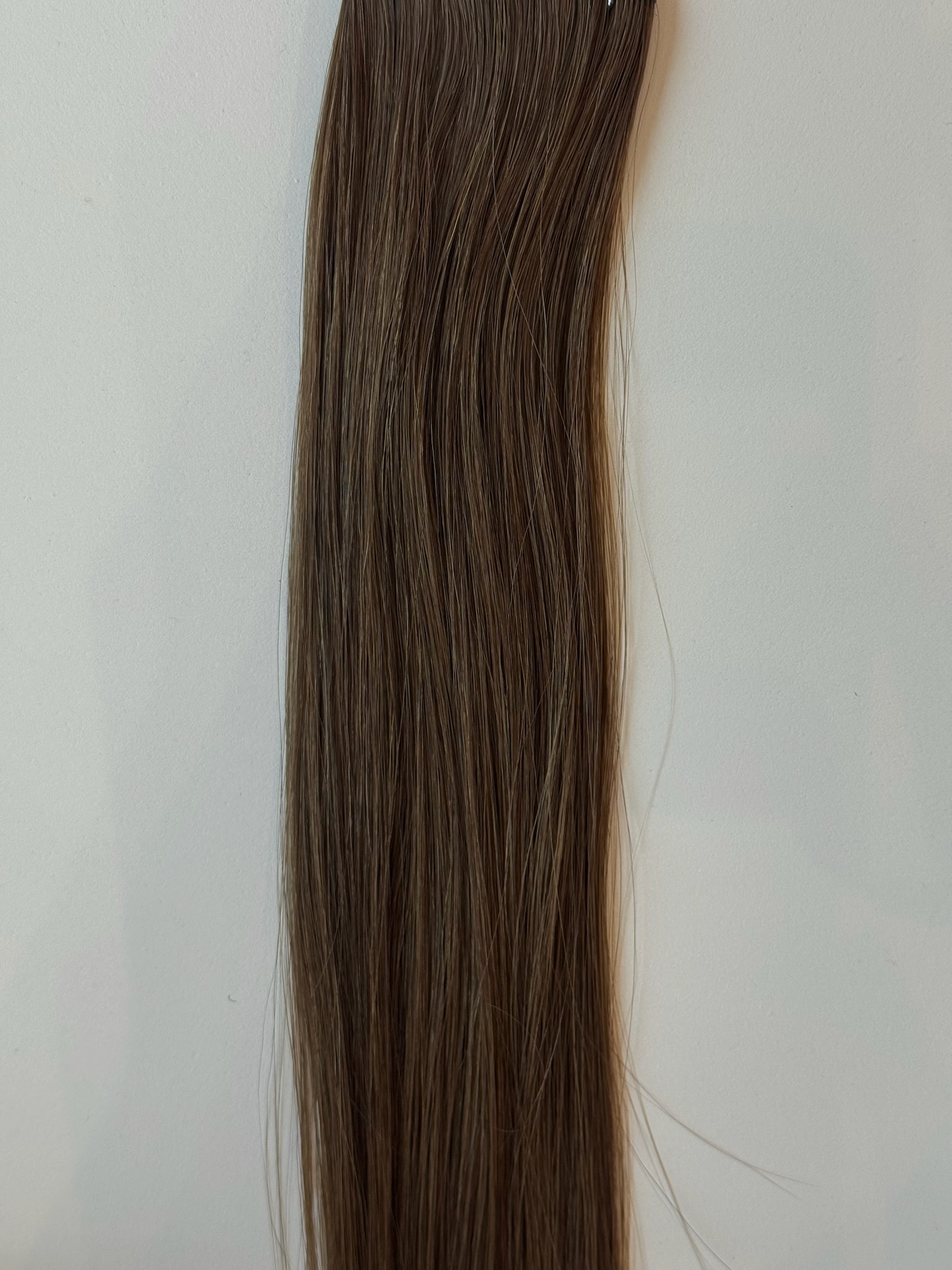 A long, straight lock of Lexi medium brown hair against a plain, light-colored background.