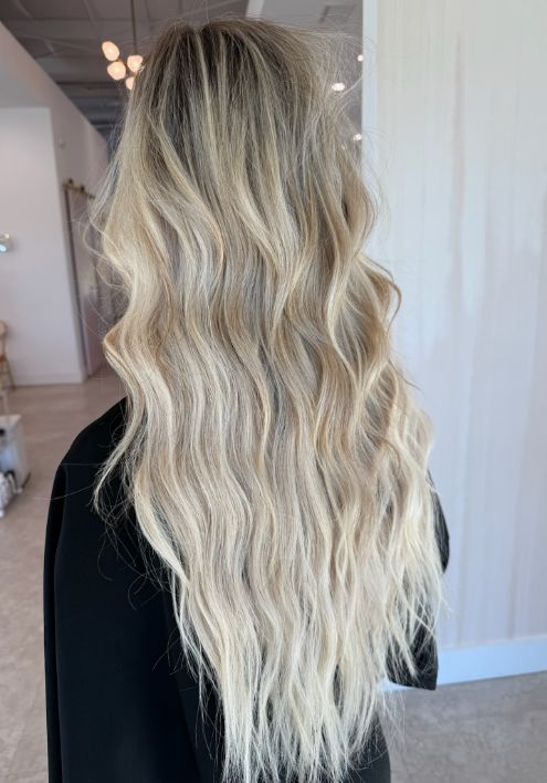 Blonde hair styled in long, luxurious waves, enhanced with elegant hair extensions for added volume and glamour.