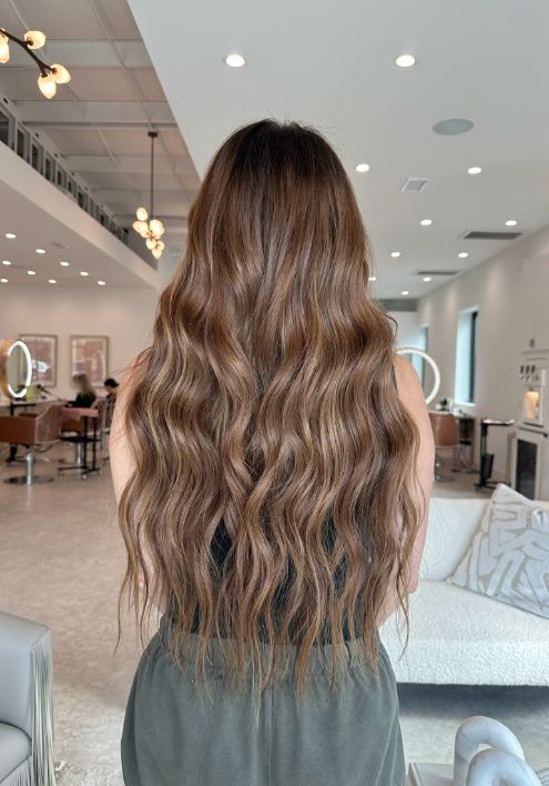 A woman with long, wavy hair viewed from the back, showcasing her elegance and the luxurious Keune Products.