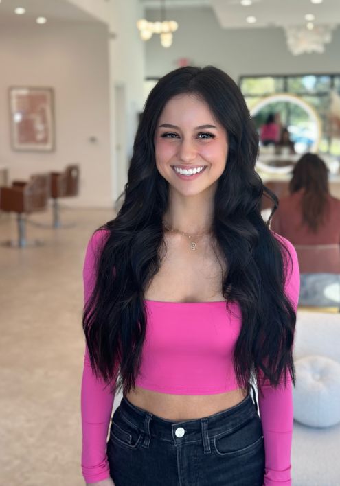 A woman in a stylish pink crop top and jeans, showcasing Luxe Hair Artists' elegant aesthetic.