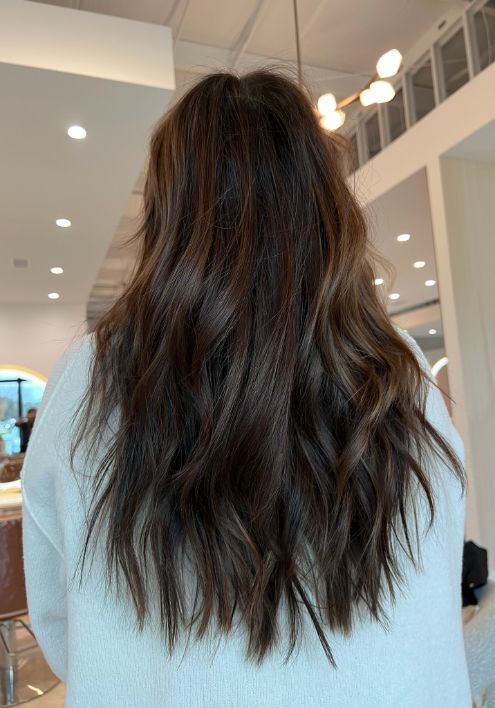A woman's back view showcasing long, wavy hair, set against the elegant backdrop of Signature Experience Salon.